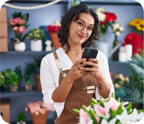 Mujer emprendedora sonriente en su floristería usando celular para recibir pagos con Poket